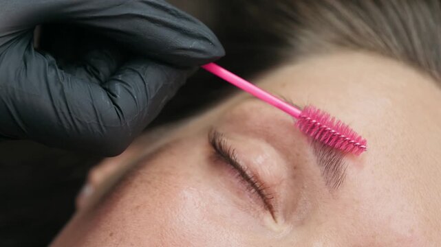 Close up of a beauty specialist brushing a clients eyebrow with a spoolie brush during a professional eyebrow shaping procedure.