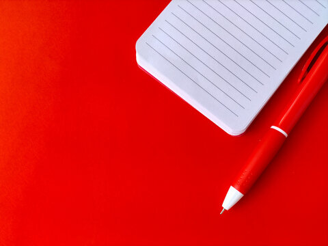 Small white spiral notebook with lined pages placed next to a matching red ballpoint pen.