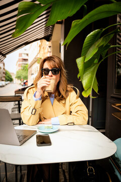  Blonde woman drinking coffee at an outdoor caf&eacute; and using her laptop