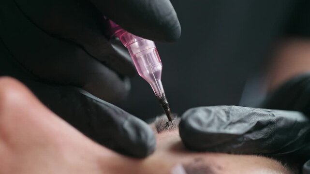 Macro close up of a permanent makeup needle with black pigment during an eyebrow tattoo procedure in a professional beauty studio.