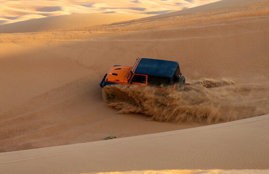Al Dhafra Region, Abu Dhabi, United Arab Emirates - 16 November 2018: View of an orange off-road vehicle driving through the sand dunes of the Liwa desert, kicking up sand while navigating.