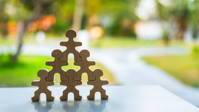Teamwork and business hierarchy concept with wooden human figures stacked in pyramid structure on table against green nature bokeh background for leadership, unity and corporate foundation.