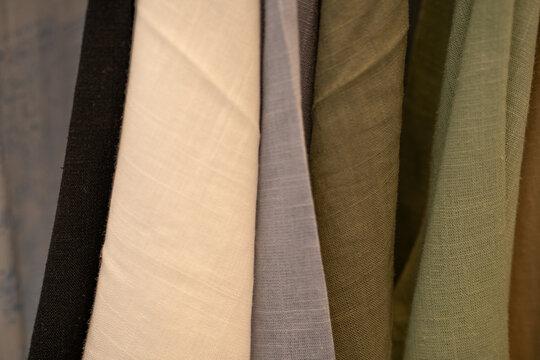 Close up of neutral fabric swatches hanging in fashion studio. Natural textile texture. Sustainable clothing design, ethical sourcing and conscious material selection. Sustainable fashion materials.