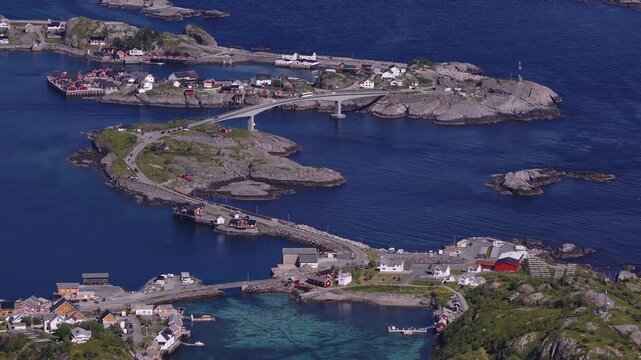 An aerial wide shot of road bridges, causeways, and coastal houses linking rocky islands across Reinefjorden in Reine, Lofoten, Norway on a bright day.