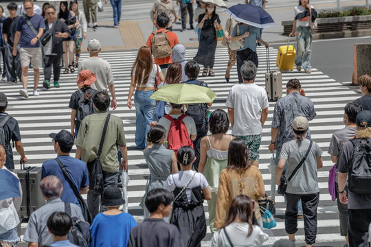 Bright lime green sun umbrella among a crowd of pedestrians crossing a busy city crosswalk in Japan on a hot summer day.