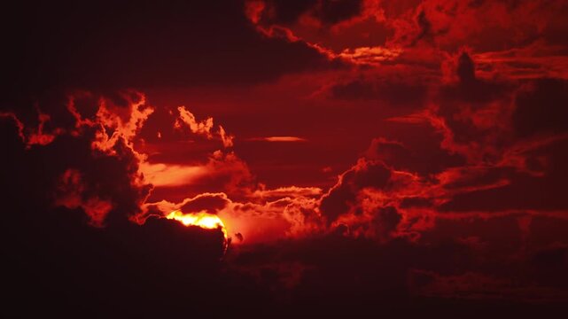 Dramatic deep red sunset time lapse with the large glowing sun disc breaking through moving clouds. 