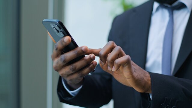 Close up unrecognizable African American business man using mobile phone near window businessman with telephone male hands holding device guy employee specialist agent browsing smartphone indoors