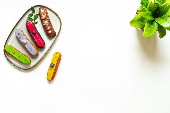 Colorful gourmet eclairs with glazed topping on plate - modern pastry flat lay in soft natural light, top view dessert concept