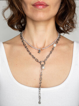 Stylish woman in white top wearing pearl and steel chain - modern minimalist jewelry fashion portrait in natural light