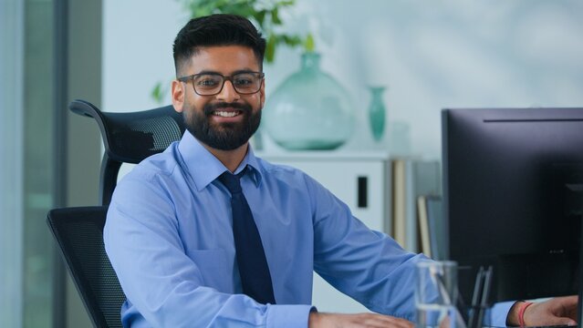 Happy Muslim business man Arabian male typing computer smiling looking at camera in office worker Indian businessman male productive executive specialist working with desktop work smile satisfied