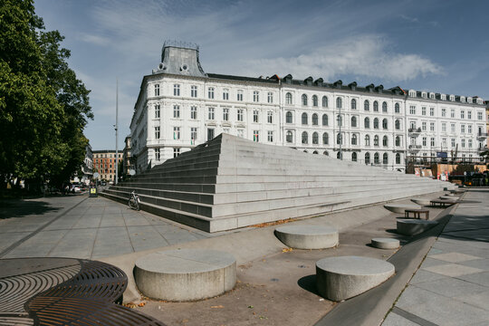 Copenhagen, Denmark - 23 August 2026: View of the modern stone steps and circular seating elements of Axeltorv square, set against a historic white building under a clear blue sky.