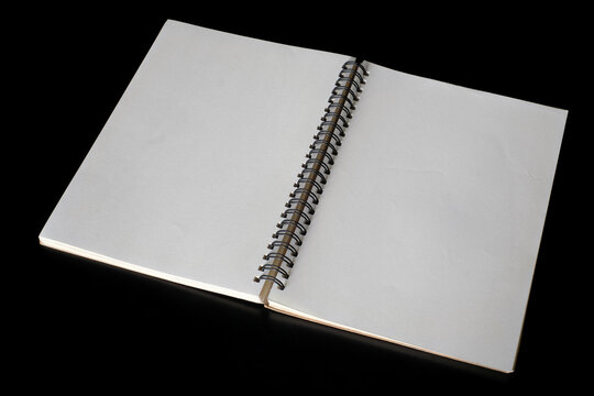 High angle studio shot of an open blank spiral notebook resting on a black background under clean lighting, symbolizing a fresh start and educational concepts.