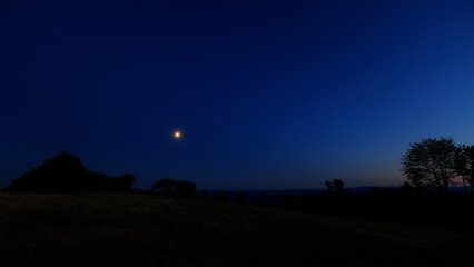 Moon on a twilight sky with stars, planets and landscape mountain silhouettes. © astrosystem