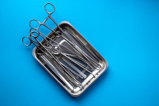 Sterile surgical instruments and tools - scalpels, scissors and others - in a stainless tray on blue background, top view