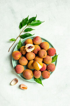 Fresh lychee fruit with green leaves on a plate, top view