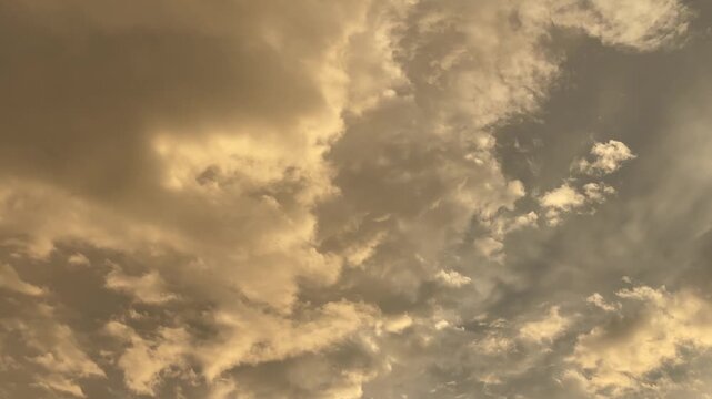 upward panorama of layered cumulus and stratocumulus clouds tinted warm golden-beige by low sun, showing localized brightening, light shafts, and shadowed cores