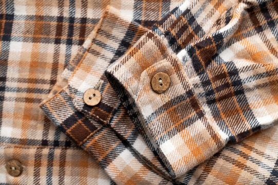 Close-up of details of plaid flannel fall shirt. Buttons, collar, sleeves, cotton plaid fabric in brown, red, beige tones. Fashionable, stylish clothing concept, texture of cozy fabric.