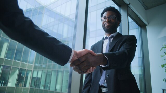 African American business man communicate shaking hands with unknown male in corporate office. Ethnic businessman consulting client handshaking two multiethnic men conclude deal businessmen agreement