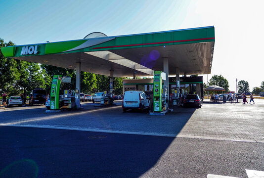 Cars parked under the spacious roof structure of a MOL gas station on a sunny day in Hungary.