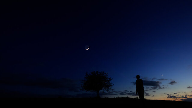 Silhouette of a person in nature observing night sky, Moon, stars and planets from a remote location.