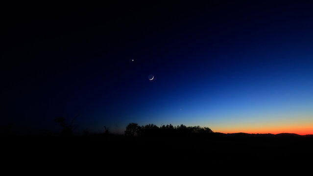 Moon on a twilight sky with stars, planets and landscape mountain silhouettes.