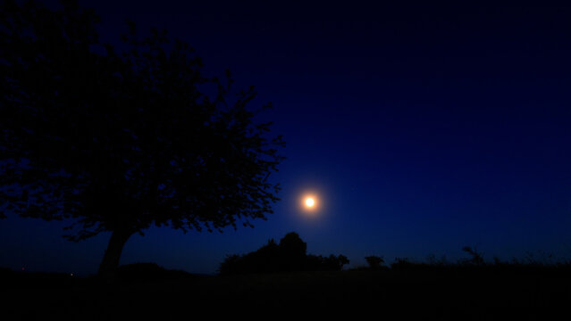 Moon on a twilight sky with stars, planets and landscape mountain silhouettes.