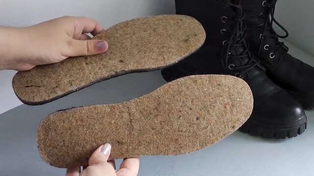 Woman holding felt shoe insoles designed to keep feet warm, boots in the background, autumn and winter footwear preparation and thermal insulation.