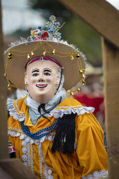 Angahuan, Michoacan, Mexico - 07 January 2024: View of a traditional Kurpites dancer wearing an ornate mask, a decorated hat with bells, and a yellow velvet jacket with lace trim.