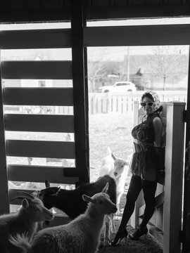 Asian woman standing barn door surrounded by goats.