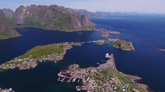 An aerial perspective shows the coastal fishing village of Reine in Lofoten, Norway, with surrounding islands, bridges, mountains, and sea.