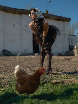 Asian woman bending forward watching chicken on farm yard
