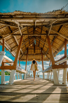 Woman tourist stay on balcony of the hut lap into the sea, relax moment on wooden pier, enjoy sunset of the summer trip in tropical island