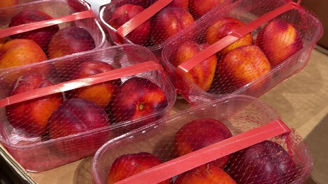 Colorful ripe nectarines are sold in small prepacked containers, offering customers an easy way to choose and carry fresh summer fruit from the market.
