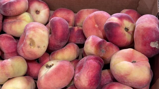 Soft donut peaches showing dark spots and early spoilage lie inside a paper box, illustrating damaged produce, food waste and reduced fruit quality during storage.