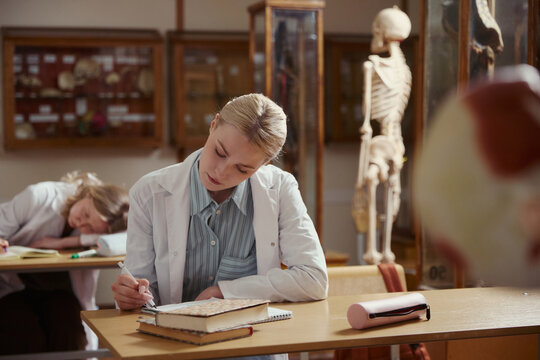 Caucasian young adult female medical student writing in notebook during anatomy class. Image represents higher education and is suitable for university promotional materials