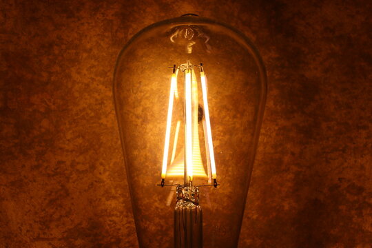 Glowing Vintage LED Filament Light Bulb on Warm Rustic Copper Background