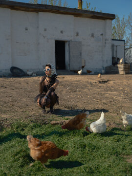 Asian woman crouching on farm yard watching chickens