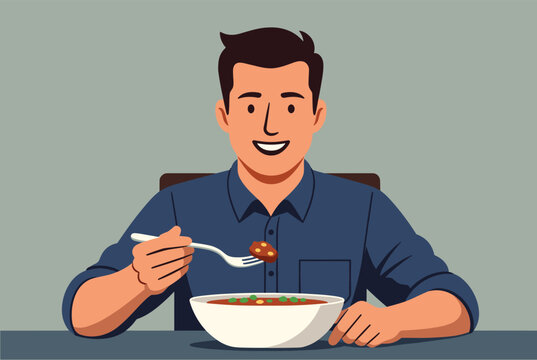 Smiling young man sits at a dining table and happily eats a warm bowl of soup using a fork to pick up a meatball.