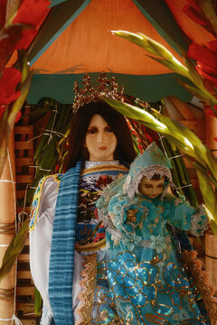 San Lorenzo, Michoacan, Mexico - 10 August 2026: View of a religious statue of the Virgin Mary and Christ child adorned with red gladiolus flowers and traditional clothing during a festival.