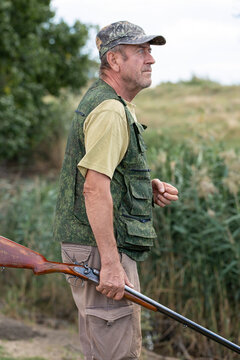 A hunter with a gun in camouflage clothing. A senior man with a gun, medium shot, searching for game.