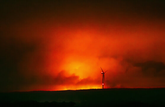 wind turbine in front of dangerous huge forest fire because of extreme weather change.