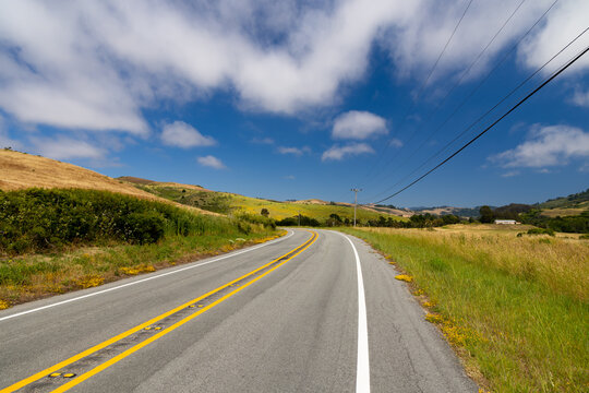 Scenic two lane road curves through golden and green grassy hills in California