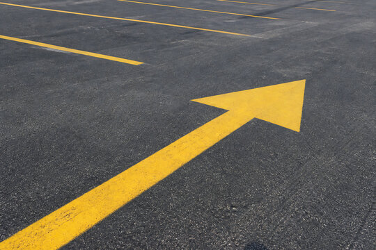 A bright yellow arrow painted on dark asphalt pavement indicating a direction.