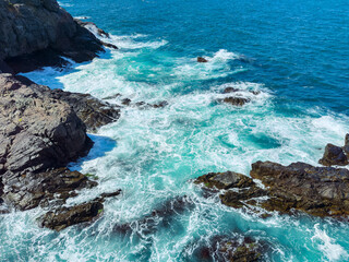 Waves crash against rocky shore under clear blue sky near ocean in bright daylight © DSMT