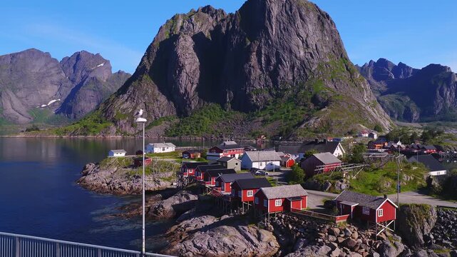 Aerial view of the coastal village of Hamnoy in Lofoten, Norway, showing traditional rorbuer cabins set along rocky shores beneath towering mountains.