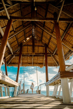 Woman tourist stay on balcony of the hut lap into the sea, relax moment on wooden pier, enjoy sunset of the summer trip in tropical island
