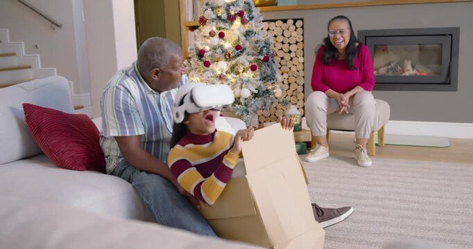 African American family at home steadying youth in box wearing white VR headset, trying VR ride