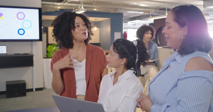Diverse women team responding to right woman holding laptop, reviewing slides and nodding in office