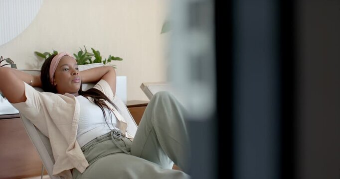 African woman reclining in lounge chair at home, adjusting leg and reflecting while blur moving