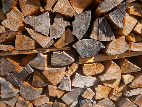 Neatly stacked split firewood logs showing natural grain, texture and warm tones. Rustic woodpile evokes cozy heating, outdoor chores, winter prep and natural materials for fireplaces.